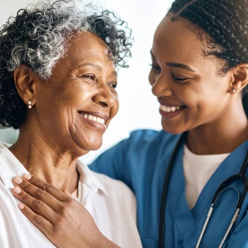 A warm and caring caregiver sitting with an elderly woman in a bright, comfortable home setting